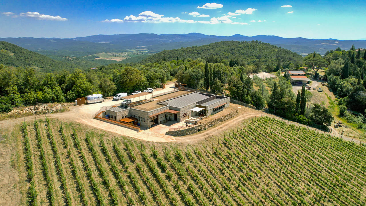 Aerial view of the I Mandorli vineyard in the Suvereto Tuscany Italy area with low modern stone buildings and in the background tree covered rolling hills extending to the horizon