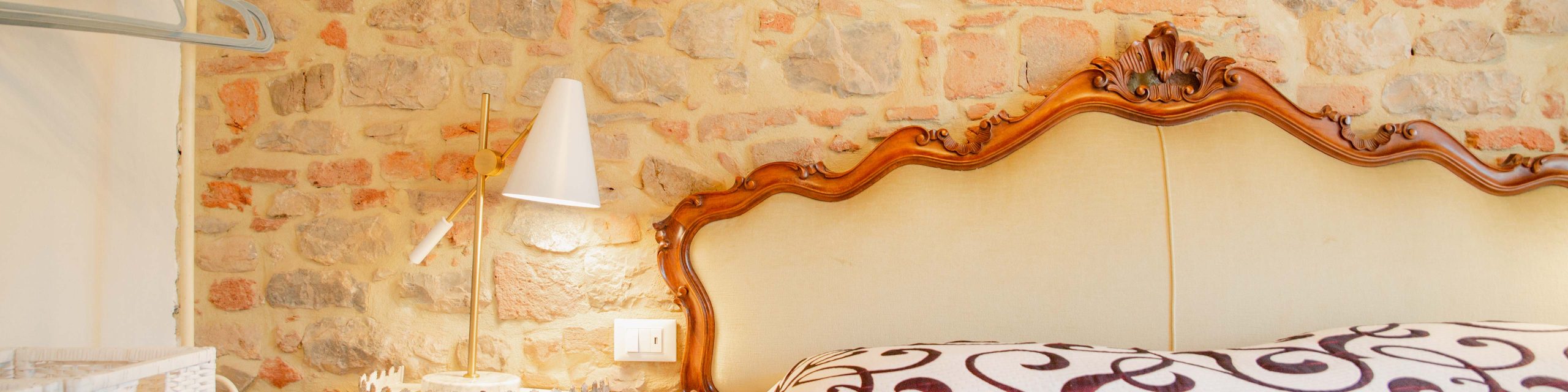 Suvereto Tuscany Vacation Properties Multicolored stone wall in a bedroom with ornate headboard of bed modern white bedside lamp
